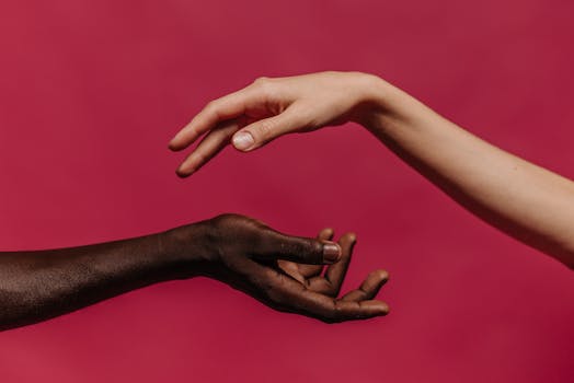 Two hands reaching towards each other against a vibrant pink background, symbolizing connection and diversity.